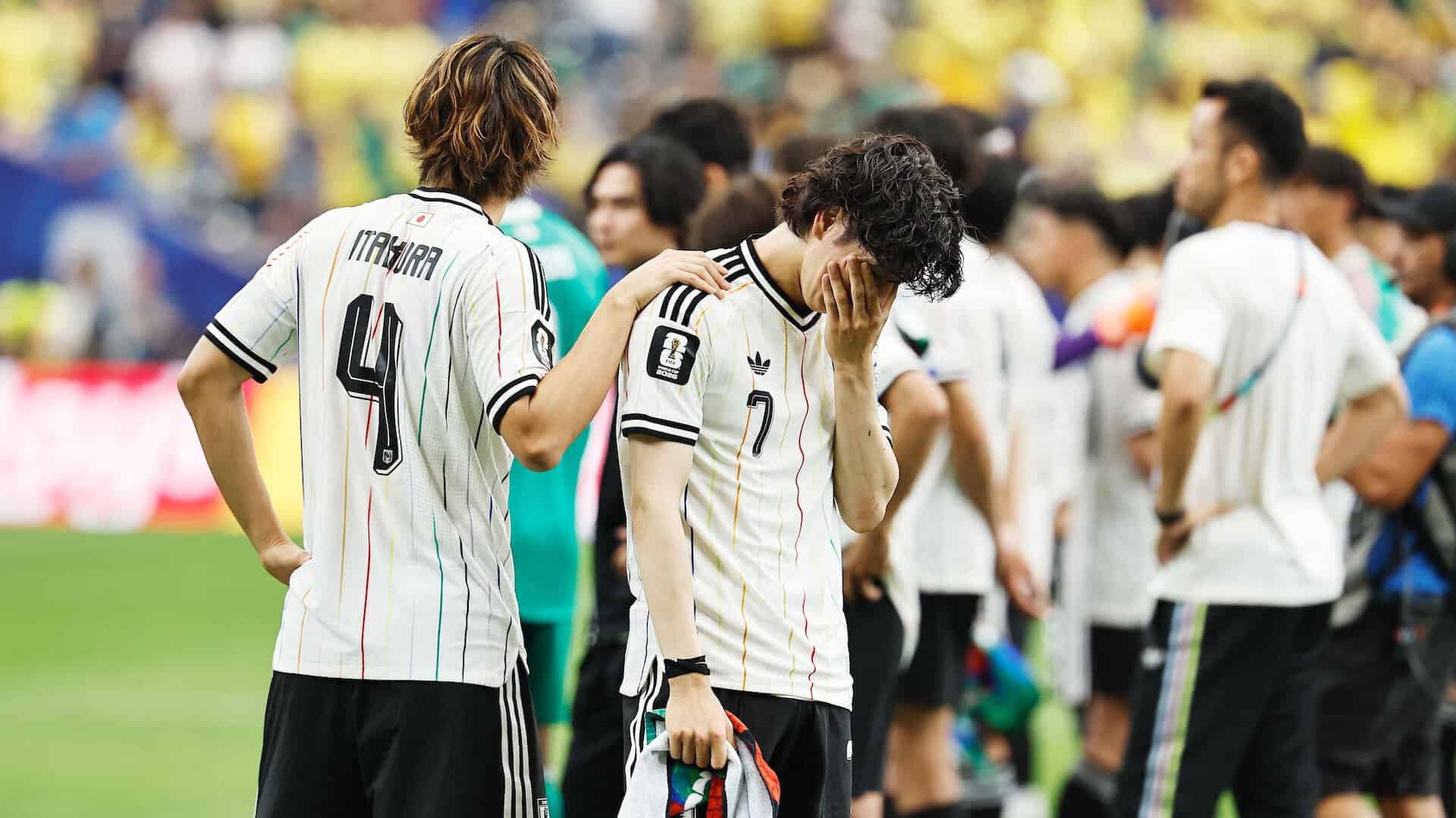 Ao Tanaka covering his face with one hand as he sobs after his late mistake led to a Brazil winner in the World Cup round of 32. A teammate has his hand on Tanaka's shoulder, looking away. On the plus side, the white kit is a beauty