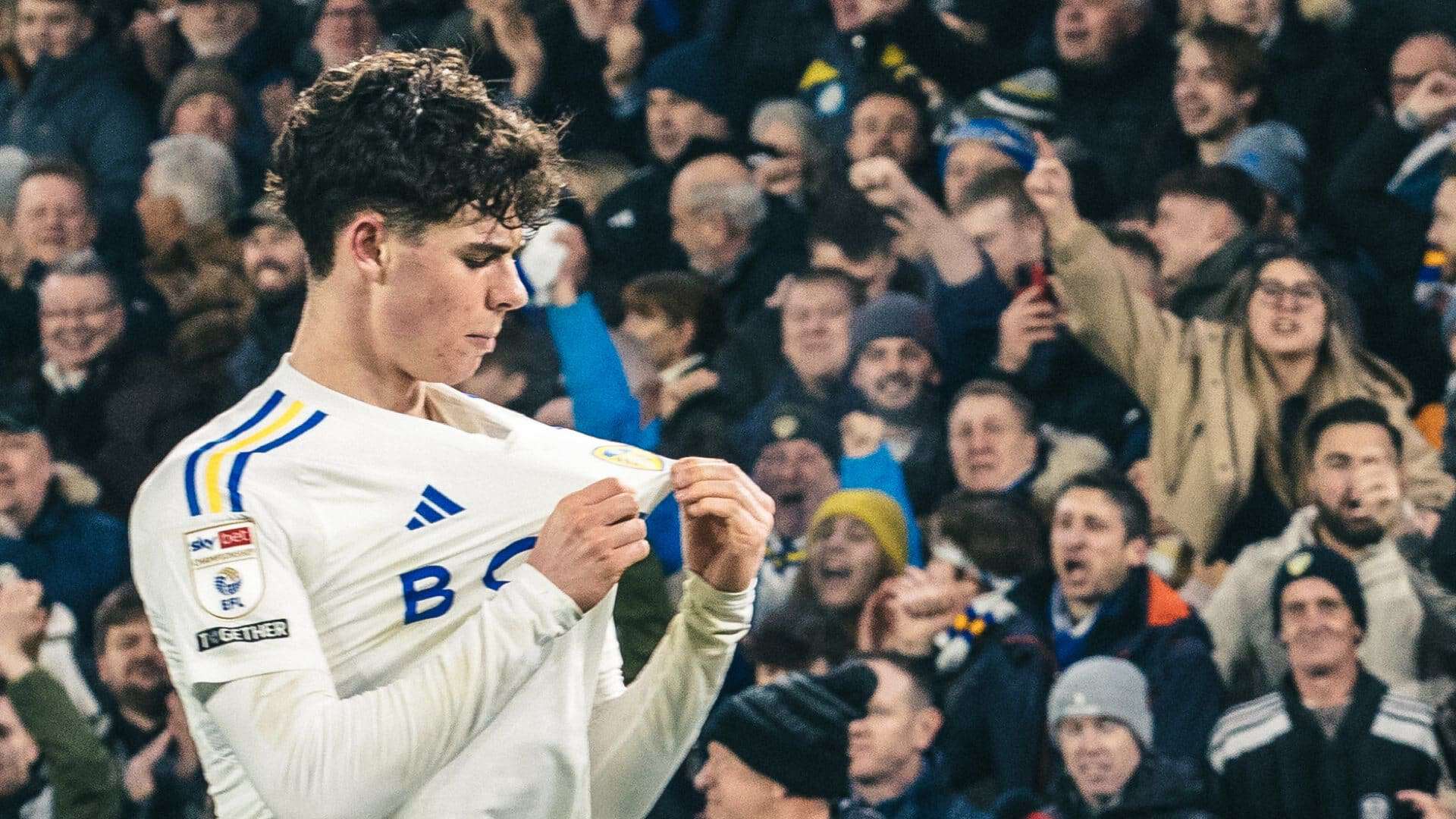 A photo of Archie Gray pulling the Leeds badge on his shirt, taken after he scored against Leicester City
