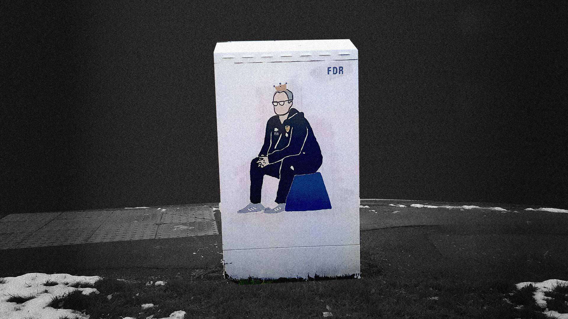 Snow melts around a painting of Bielsa on a streetside junction box