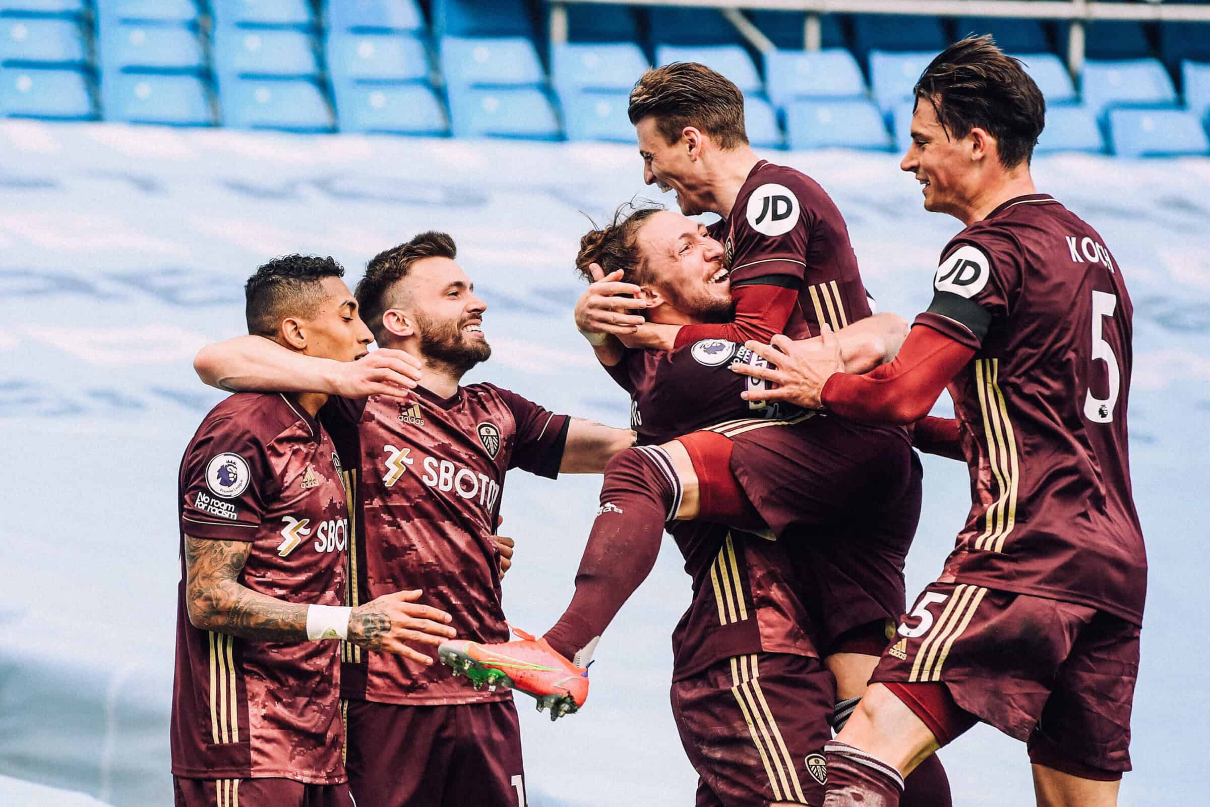 Stuart Dallas celebrating his opener at the Etihad with his arm around Raphinha while Bill Ayling catches a leaping Gjanni Alioski