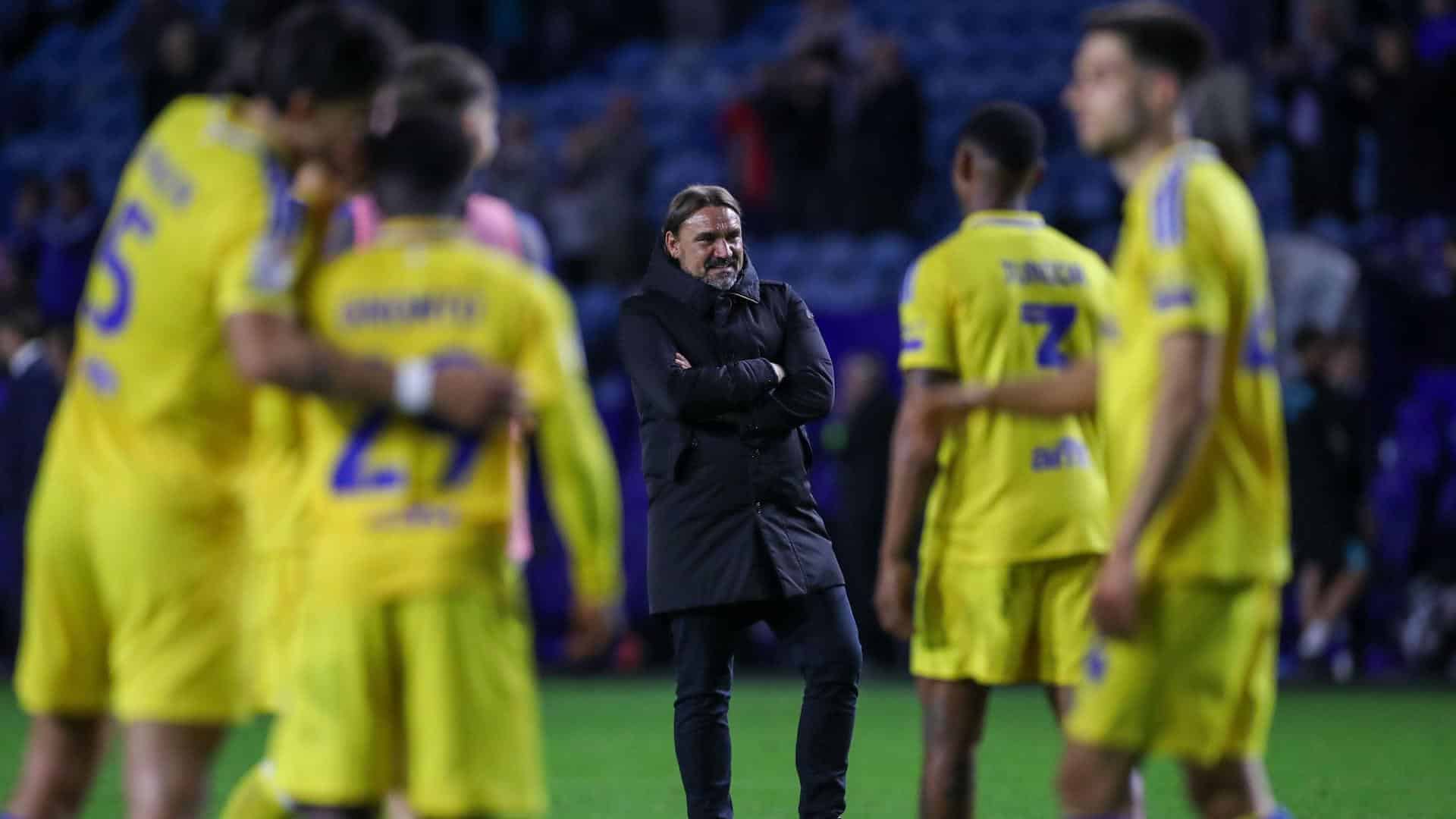 Daniel Farke stands in his big black coat looking satisfied while his players celebrate Leeds' win at Sheffield Wednesday around him