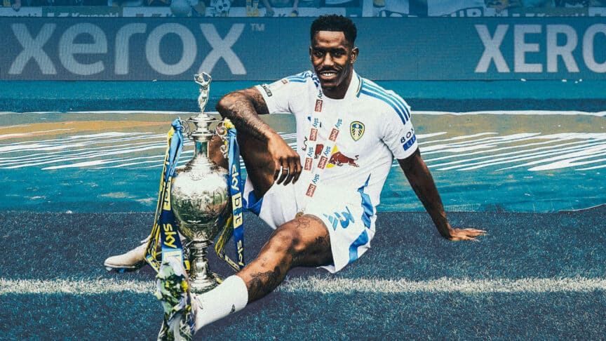 Junior Firpo sitting in front of the away end at Plymouth with a gleaming smile and a gleaming Championship trophy
