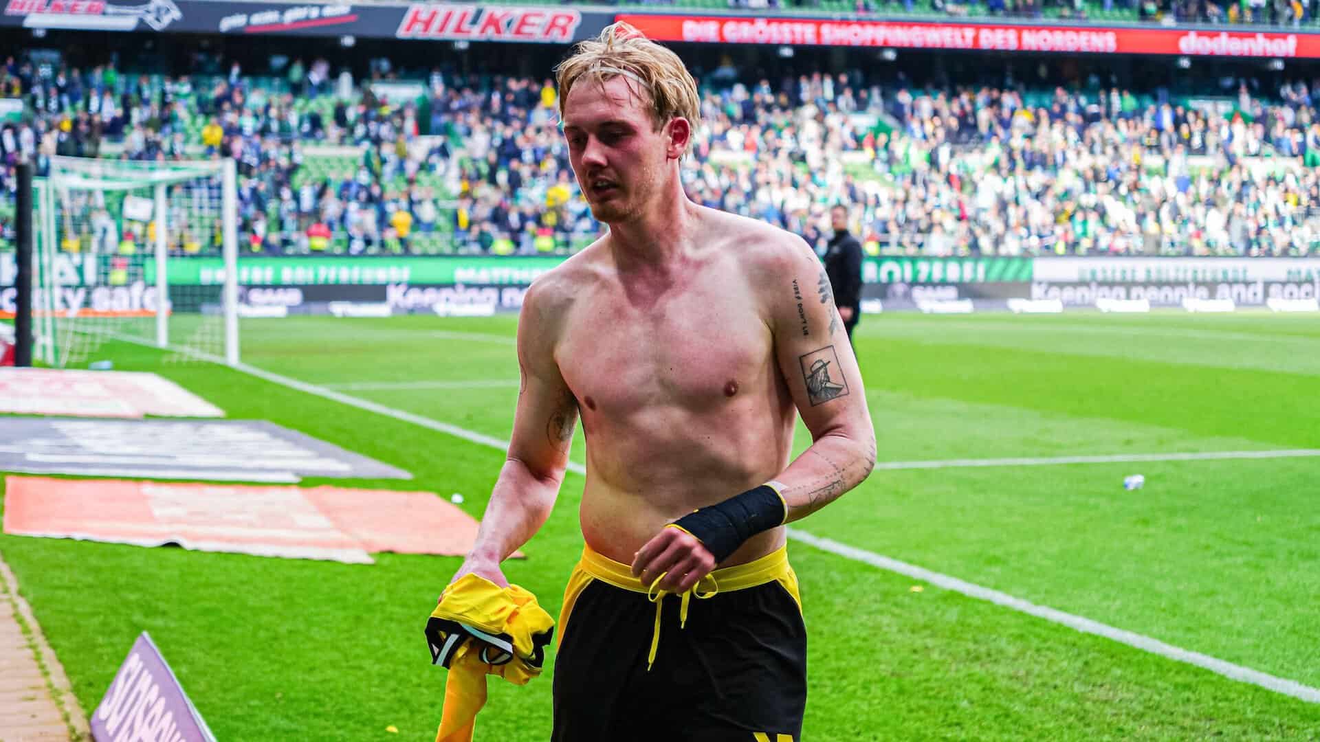 Julian Brandt with his top off, ready to hand his shirt to a Borussia Dortmund supporter at the end of the game. I can't make out his tattoos but they look cooler than most footballers'