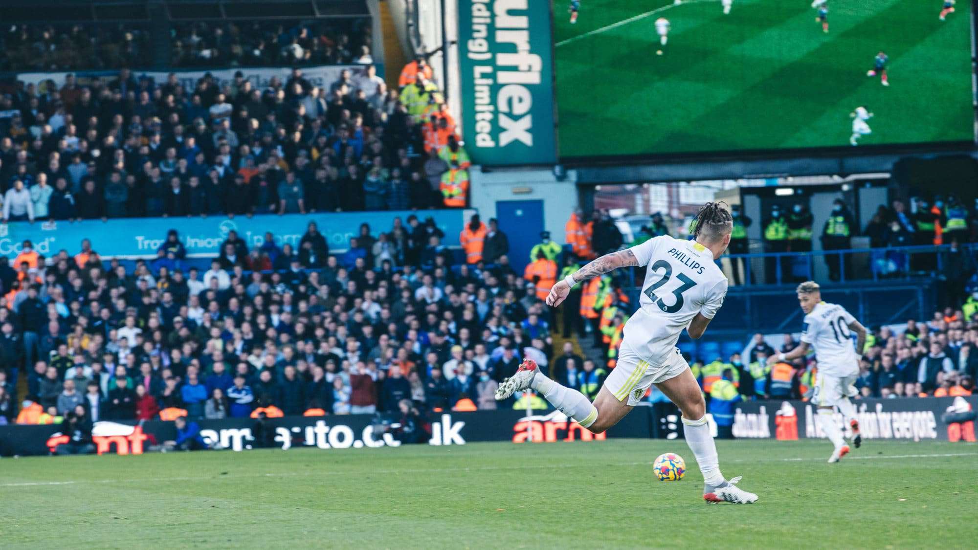 The back of Kalvin Phillips as he drills a pass down the line for Raphinha. On the big screen in the background, you can see a television view of the same thing!