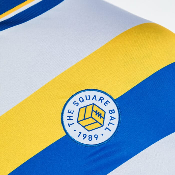 A close up view of the TSB badge on our new Admiral shirts, placed on a blue and yellow diagonal sash across a white shirt