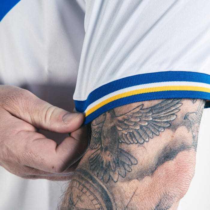 A close up view of the short sleeve cuff on our 2024 TSB x Admiral home shirt, blue with a yellow and white band on an all-white shirt