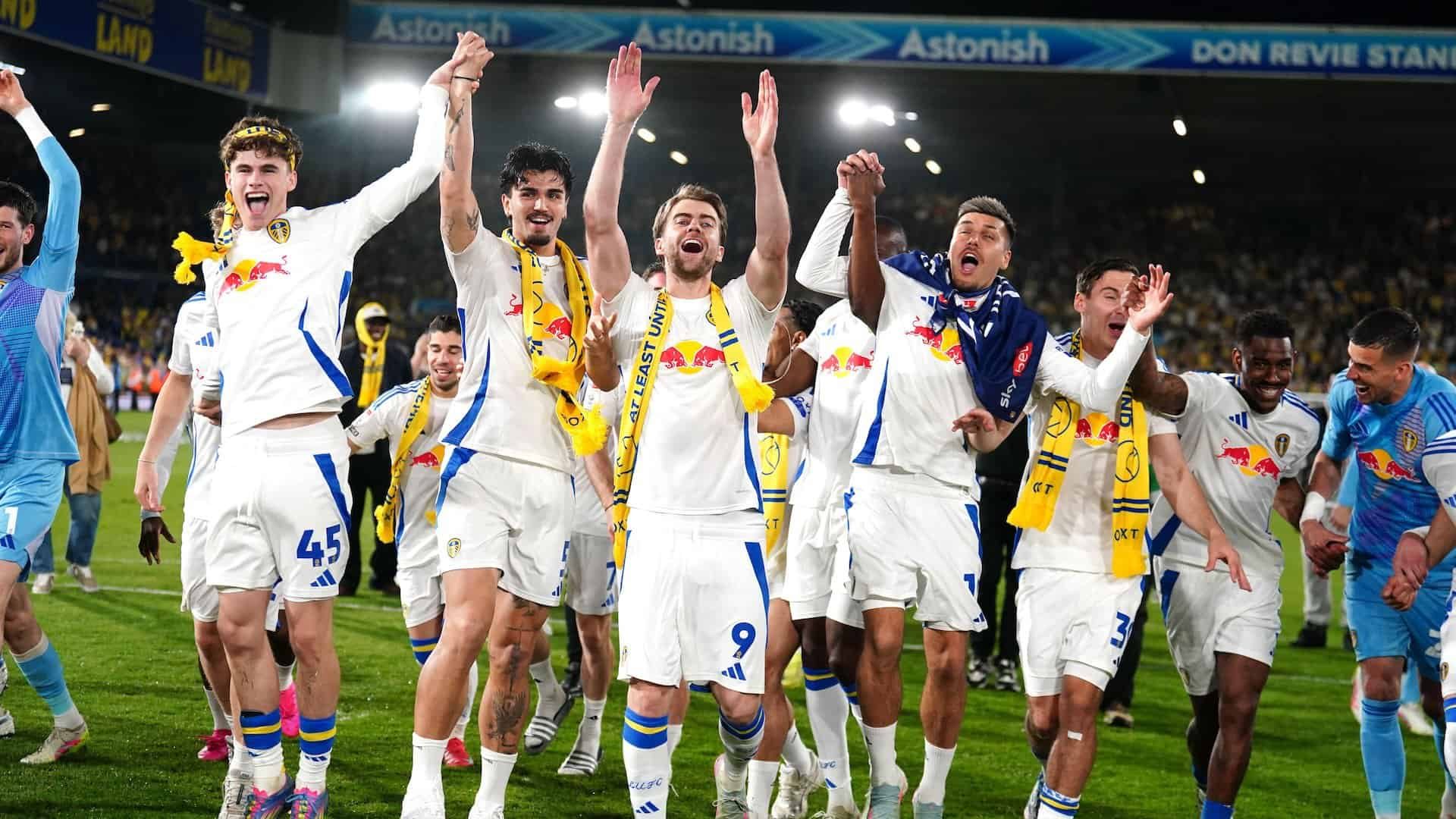 Pat Bamford, Pascal Struijk, Joel Piroe and Harry Gray with their arms in the air saluting the crowd. Piroe's got a flag over him and his eyes are shut, obviously